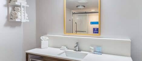 Une salle de bain moderne avec un lavabo blanc, un miroir doté d’un cadre doré et un porte-serviettes où sont soigneusement pliées les serviettes.