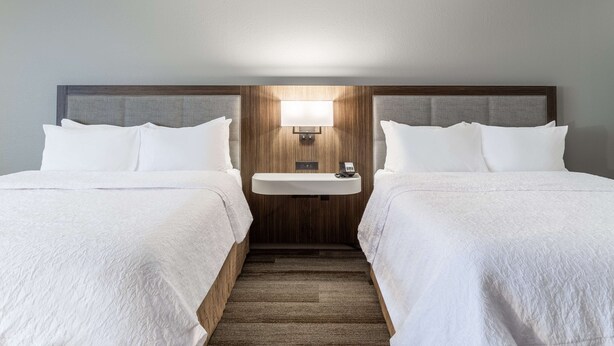 A hotel room with two beds, a small bedside table with a lamp, and a wooden headboard.