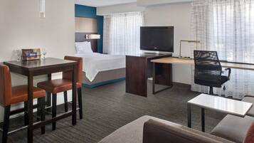 A hotel room with a bed, a desk, a television, a chair, and a sofa.