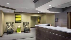 A reception area with a wooden reception desk, two patterned chairs, a green side table, and a large abstract painting on the wall. - Residence Inn Cranberry Township Pittsburgh by Marriott (Warrendale)