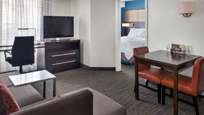 A hotel room with a TV, a desk, a dining table with chairs, a sofa, and a bed with a blue headboard. - Residence Inn Cranberry Township Pittsburgh by Marriott (Warrendale)
