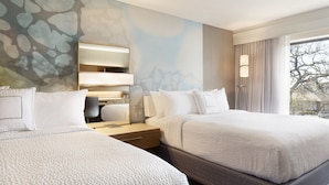 A hotel room with two beds, a large mirror, a nightstand, and a window with curtains.