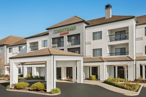 Un hotel Courtyard Marriott con un acceso cubierto, varios balcones y una entrada arbolada.