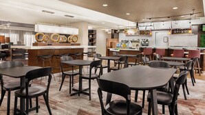 A modern cafe with multiple tables and chairs, a counter with coffee options, and a kitchen area.