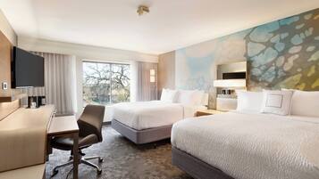 A hotel room with two beds, a desk, a chair, a flat-screen TV, and a large window.