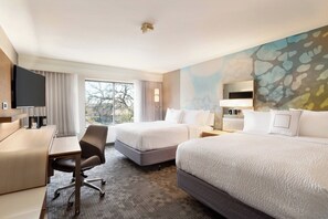 Une chambre d’hôtel avec deux lits, un bureau, une chaise, un téléviseur à écran plat et une grande fenêtre.
