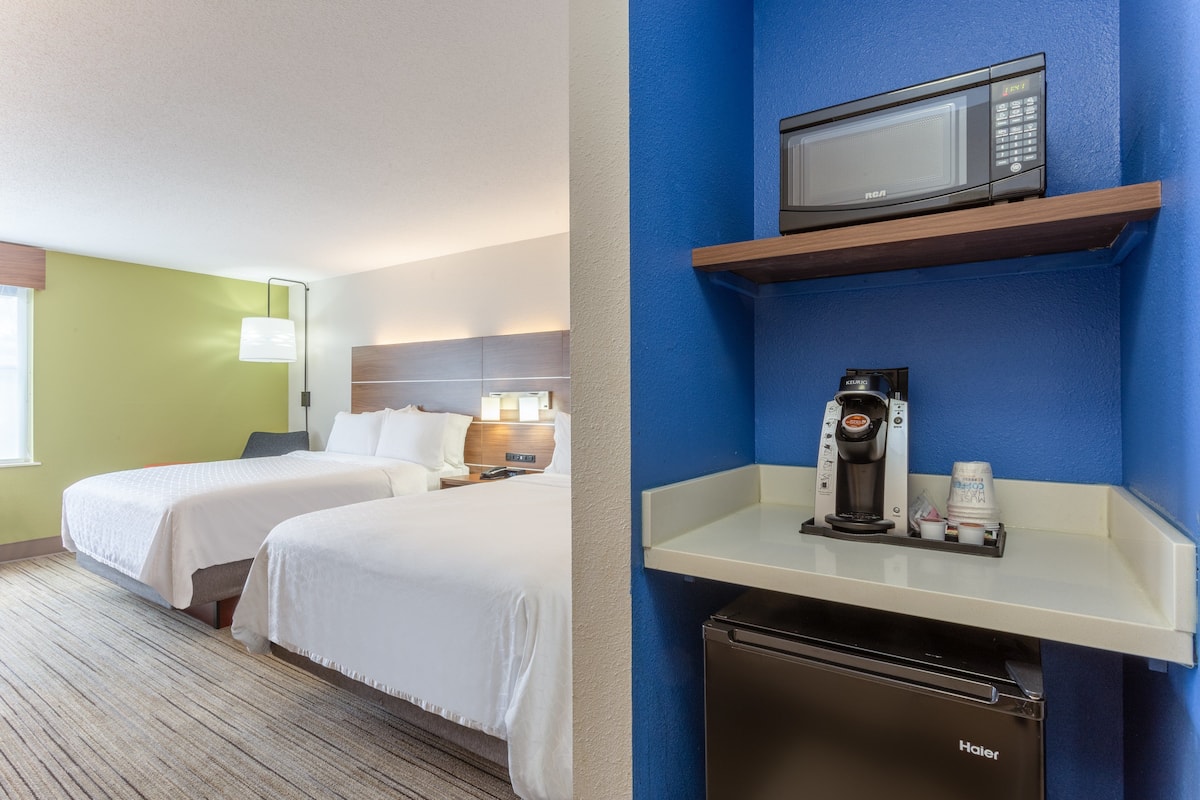 A hotel room with two beds, a microwave, a coffee maker, and a Haier refrigerator.