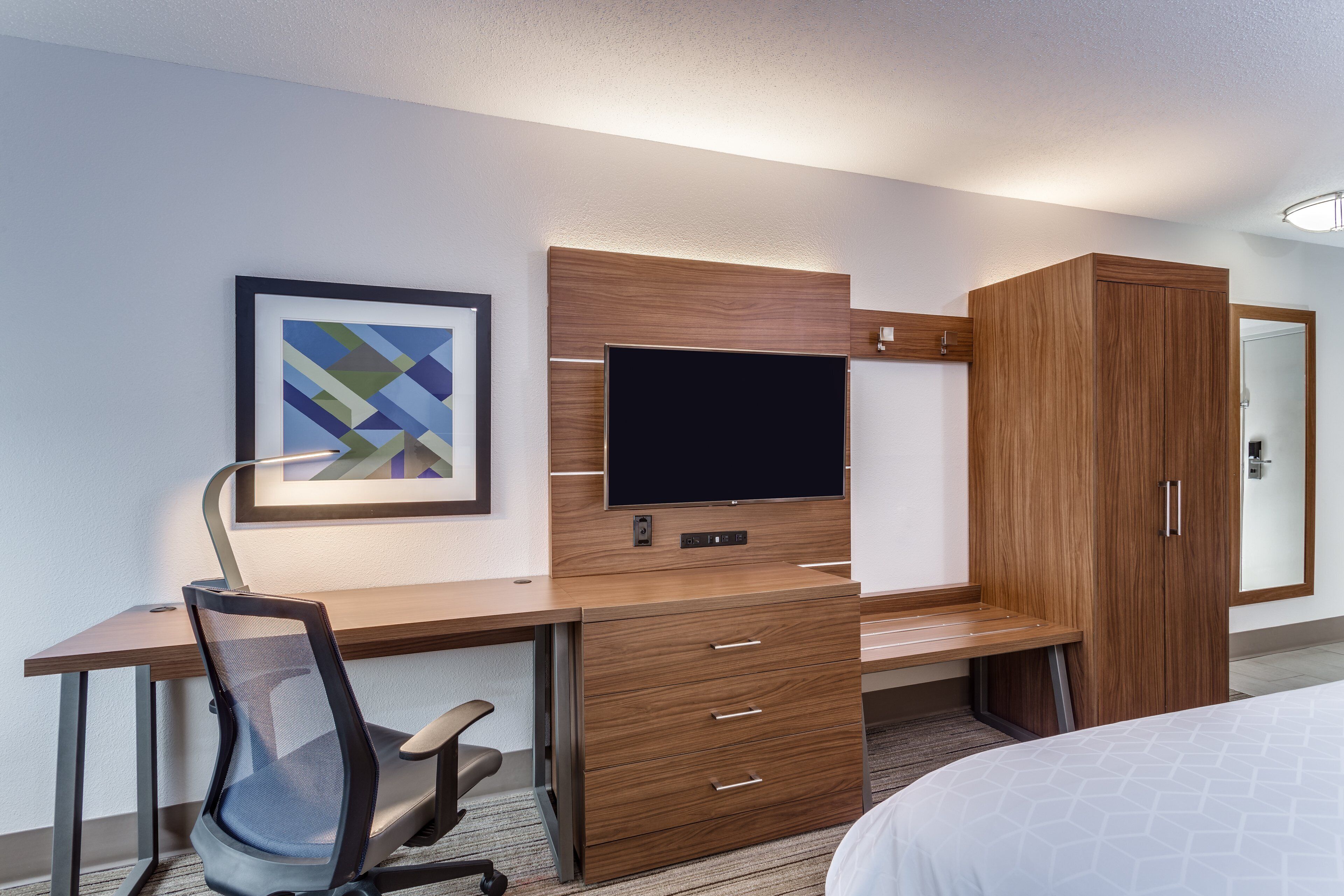 Habitación de hotel con escritorio de madera, televisión, silla, cama y armario.