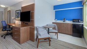 A modern hotel room with a wooden desk, a flat-screen TV, a kitchenette, and two patterned chairs. - Holiday Inn Express & Suites Scottsburg by IHG (Scottsburg)