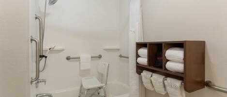 A modern bathroom with a walk-in shower, grab bars, a white bathtub, and a towel rack with neatly folded towels.