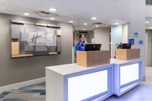 Mostrador de recepción de un hotel con pantalla digital, letrero de Holiday Inn Express & Suites y señal de registro.