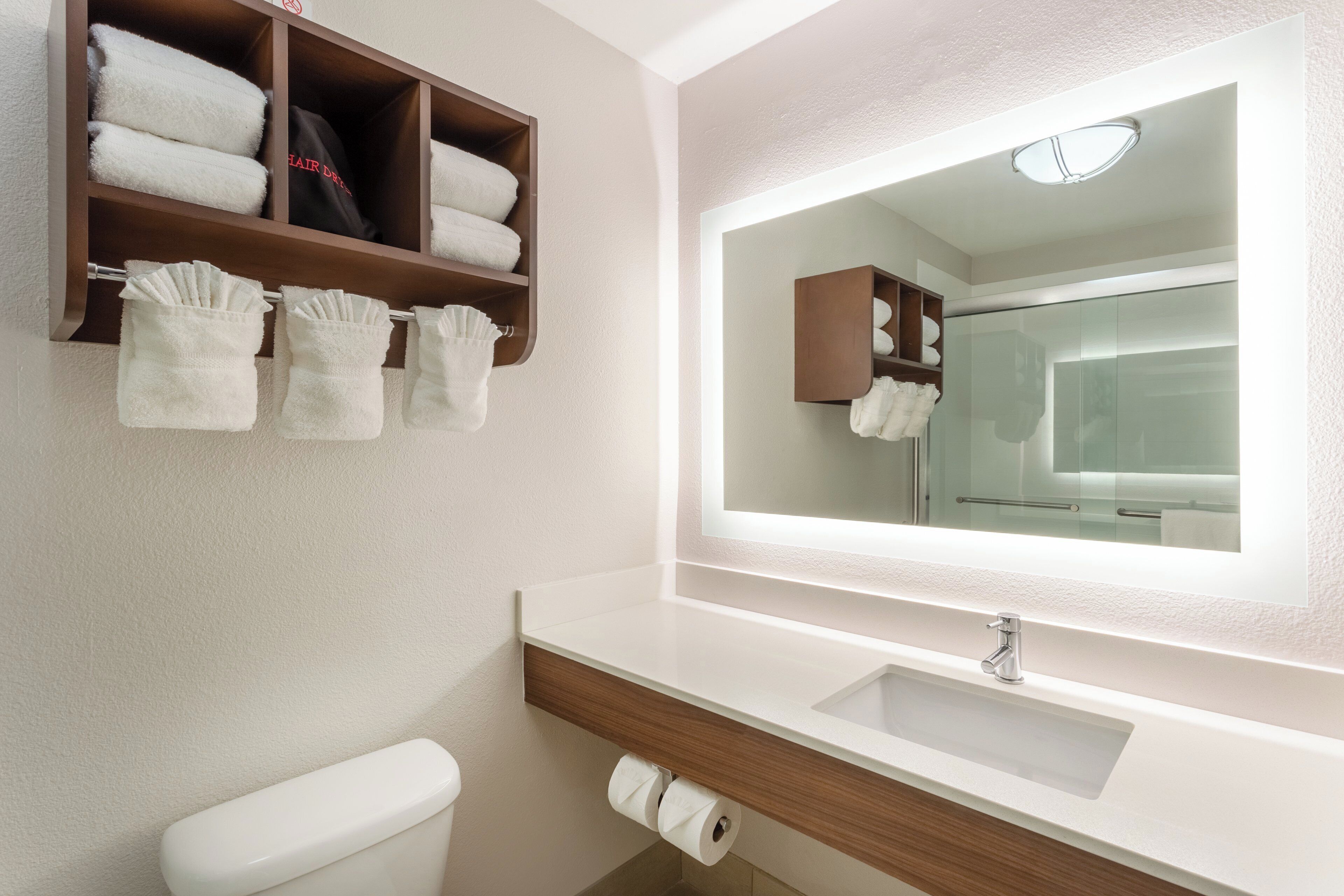Une salle de bain équipée d’un WC, d’un lavabo, d’un miroir et d’un porte-serviettes avec des serviettes pliées.