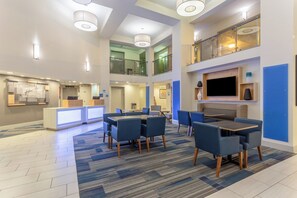 A hotel lobby with a reception desk, seating area, and a staircase leading to an upper level.