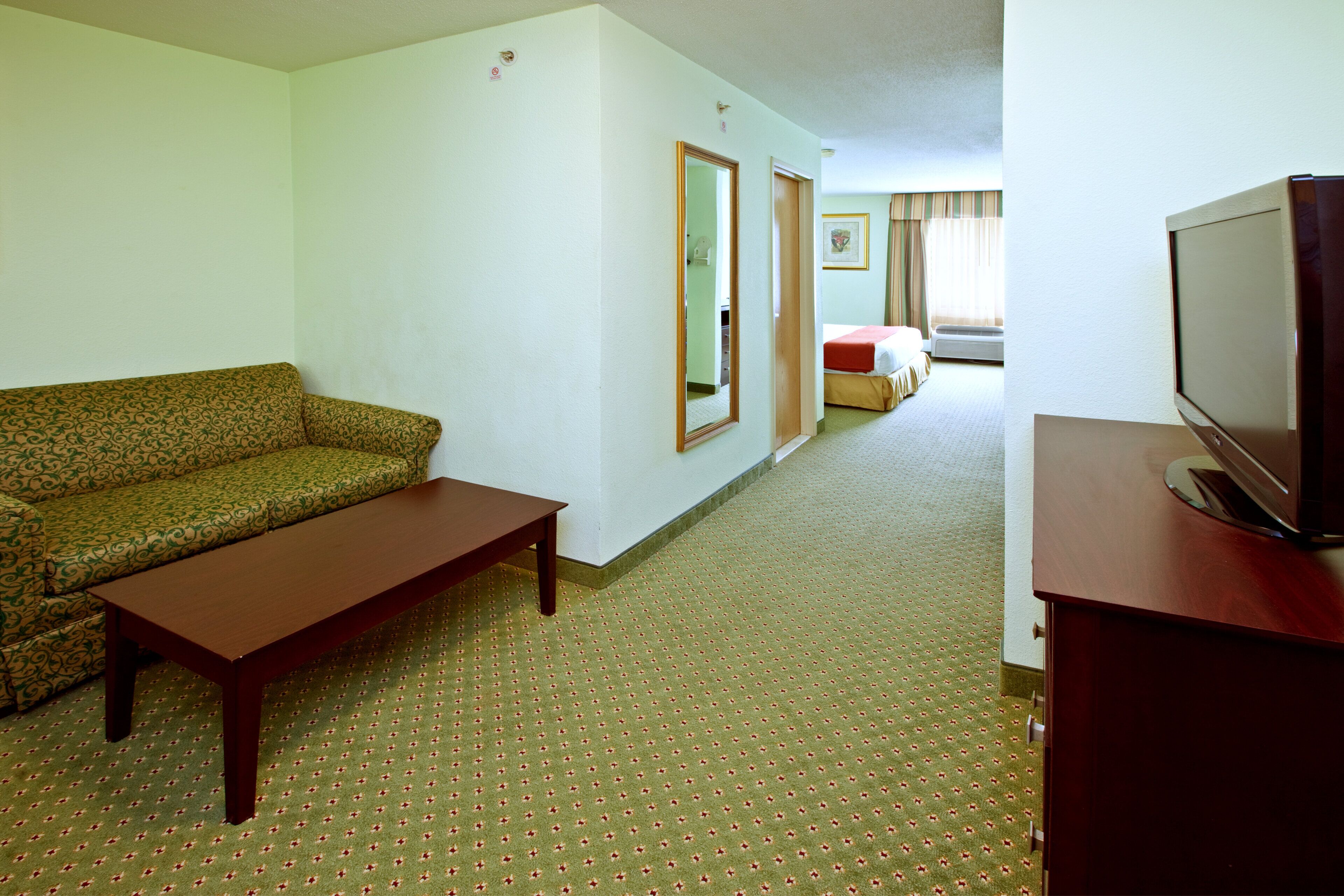 Habitación de hotel con sofá, una mesita, televisor, cama y espejo.