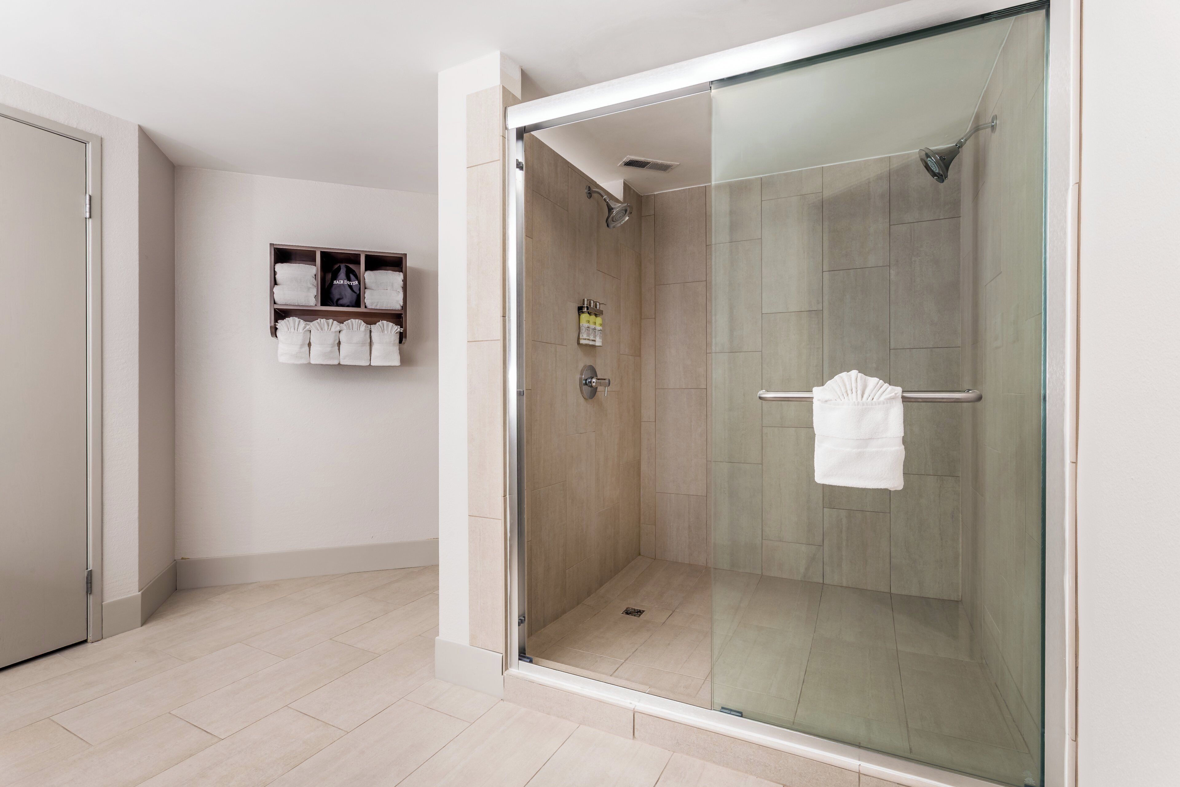 Une salle de bain moderne avec une douche à parois de verre, un porte-serviettes blanc et une étagère où sont pliés les serviettes.