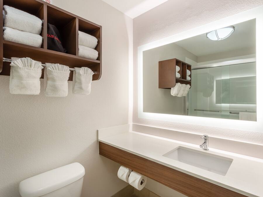 A bathroom with a white sink, a mirror, a toilet, and a towel rack with folded towels.