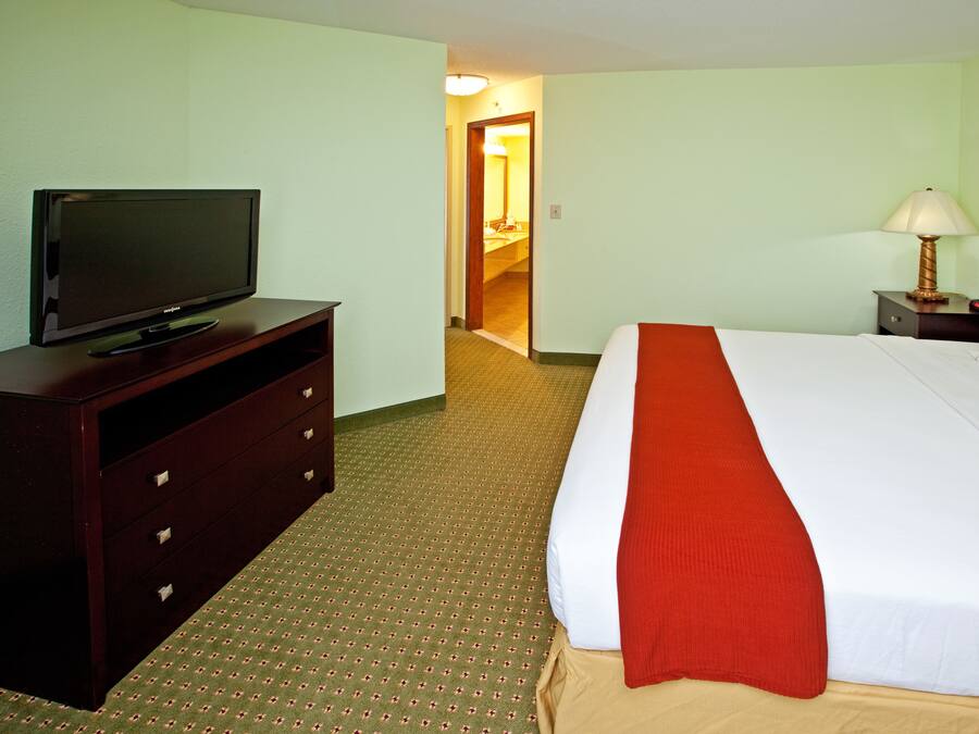 A hotel room with a bed, a television on a dresser, a lamp, and a door leading to a bathroom.