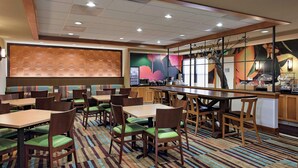 A hotel dining area with multiple tables and chairs, a bar, and a large mural on the wall.