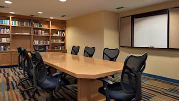 Un salón de conferencias con una larga mesa, seis sillas, una pizarra y estanterías.