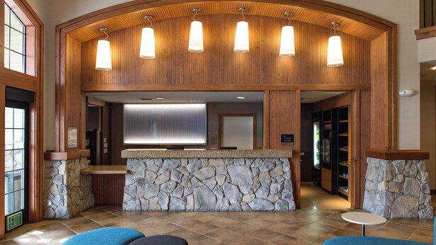 A reception area with a stone counter, wooden paneling, and a large TV screen. There are two blue chairs and a small table.