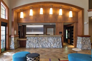 A reception area with a stone counter, wooden paneling, and a large TV screen. There are two blue chairs and a small table. - Fairfield Inn & Suites Santa Rosa Sebastopol (Sebastopol)