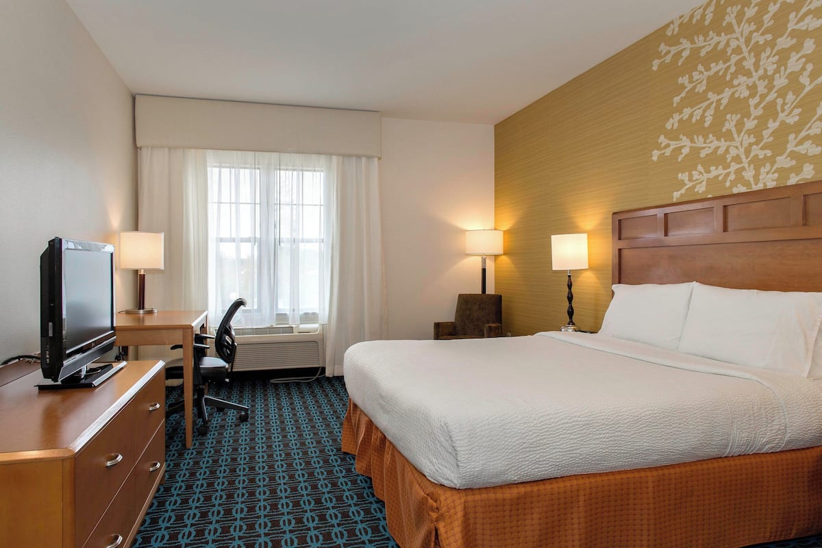 A hotel room with a bed, desk, chair, television, lamps, and a window with curtains.
