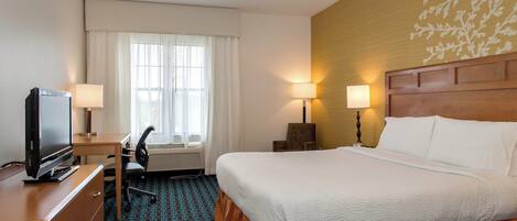 A hotel room with a bed, desk, chair, television, lamps, and a window with curtains.