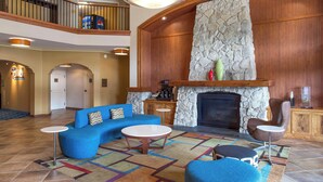 A spacious lobby with a high ceiling, a stone fireplace, a blue sofa, and a coffee table.