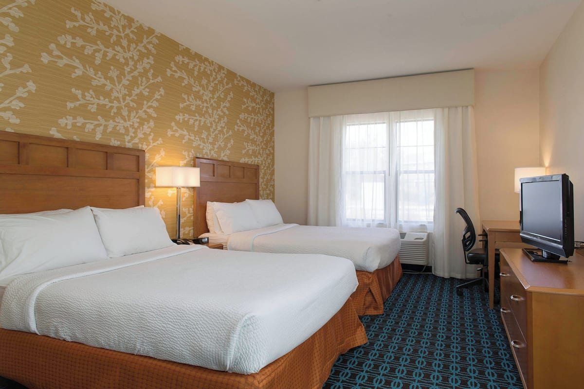 A hotel room with two beds, a television, a desk, and a window with curtains.