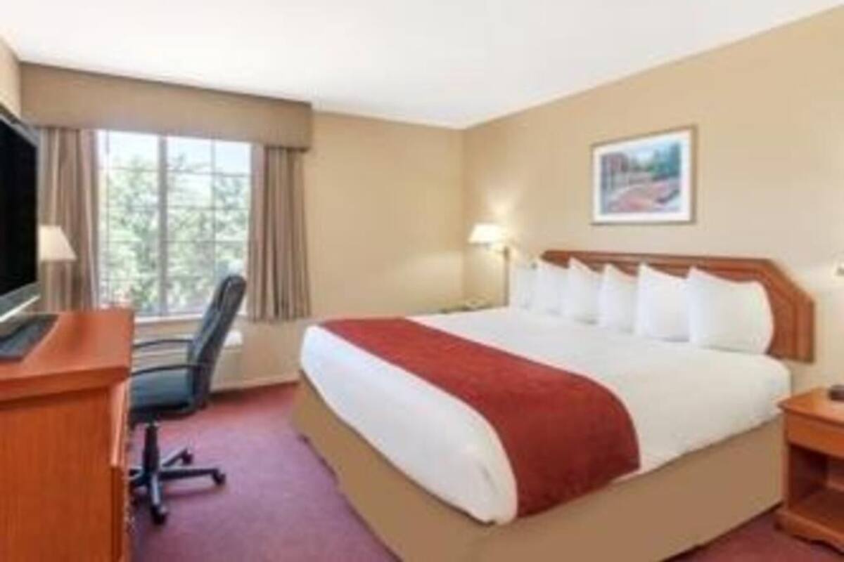 Een hotelkamer met een bed, een bureau, een stoel, een televisie en een raam met gordijnen.
