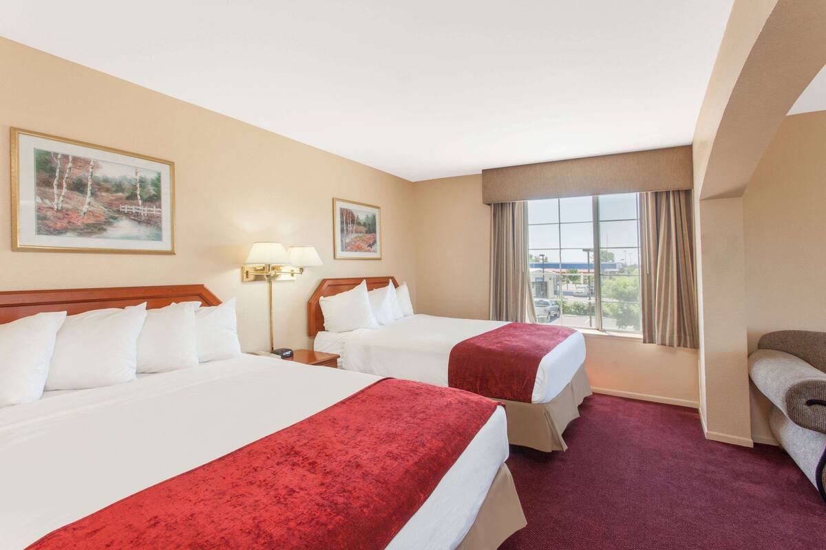 Hotelkamer met twee bedden, een slaapbank, een groot raam met uitzicht en twee schilderijen aan de muur.