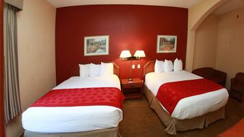 A hotel room with two beds, red and white bedding, a nightstand with lamps, and two wall-mounted paintings.