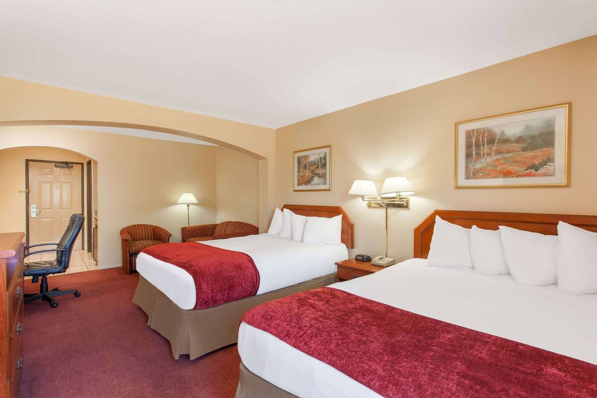 Een hotelkamer met twee bedden, een bureau en een stoel. Er zijn twee lampen en een schilderij aan de muur.