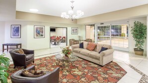A spacious living room with a large sofa, a coffee table, and a patterned rug. There is a chandelier, a potted plant, and a view through a glass door. - Ramada by Wyndham Fresno Northwest (Fresno)