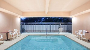 A swimming pool with a view of trees at dusk, surrounded by white chairs and a table. - Ramada by Wyndham Fresno Northwest (Fresno)