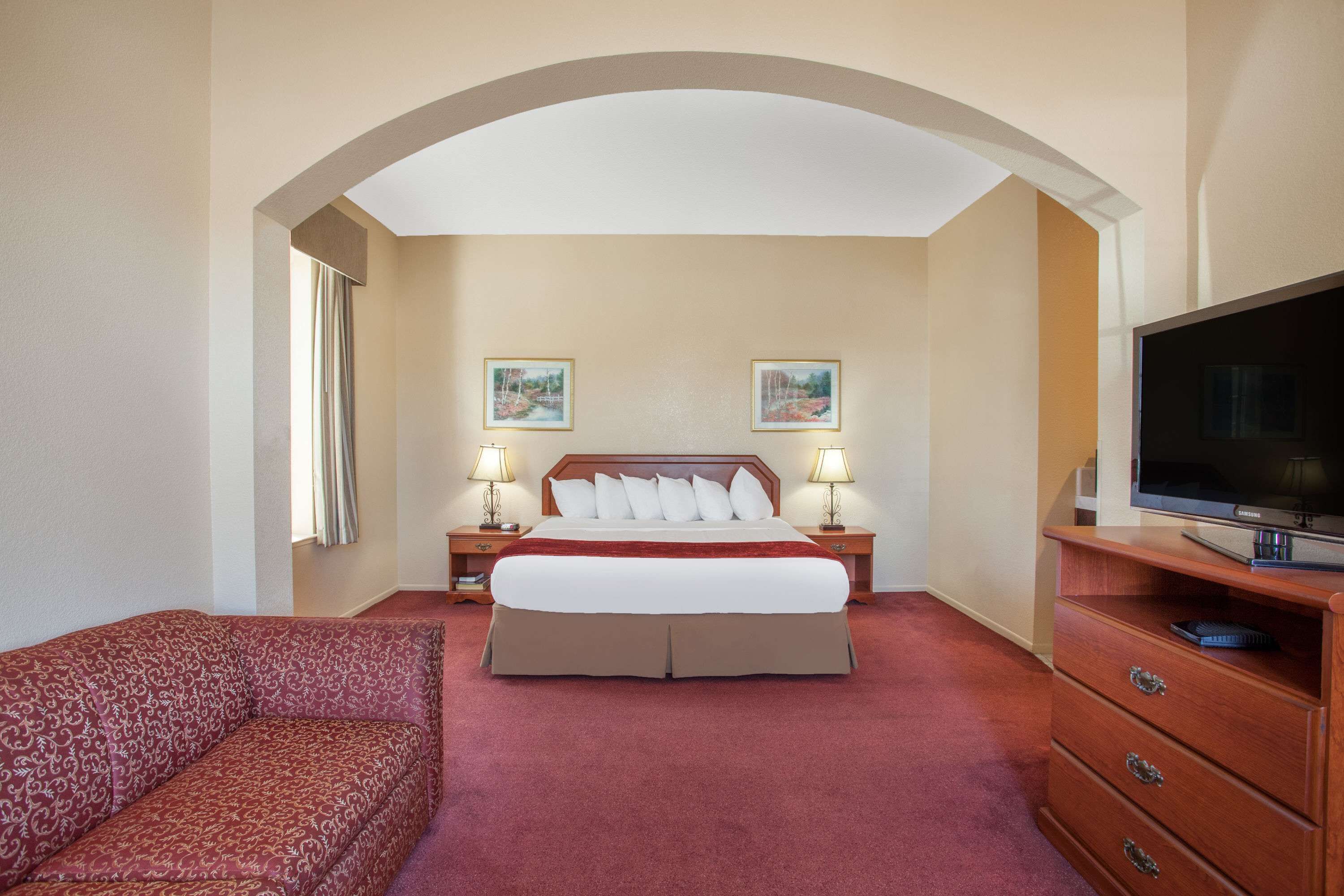 A hotel room with a large bed, two bedside lamps, a television, and a sofa.