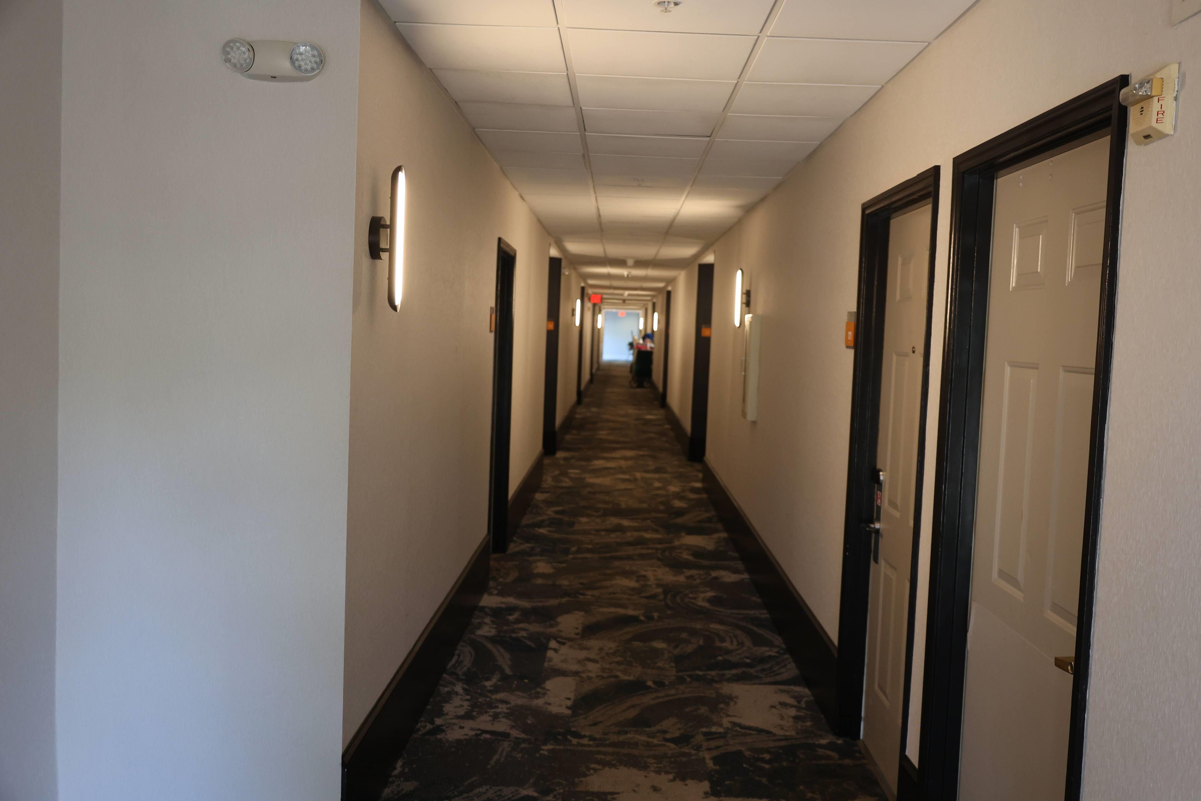 Un couloir d'hôtel avec des revêtements de sol en moquette, des portes des deux côtés et un éclairage au plafond.