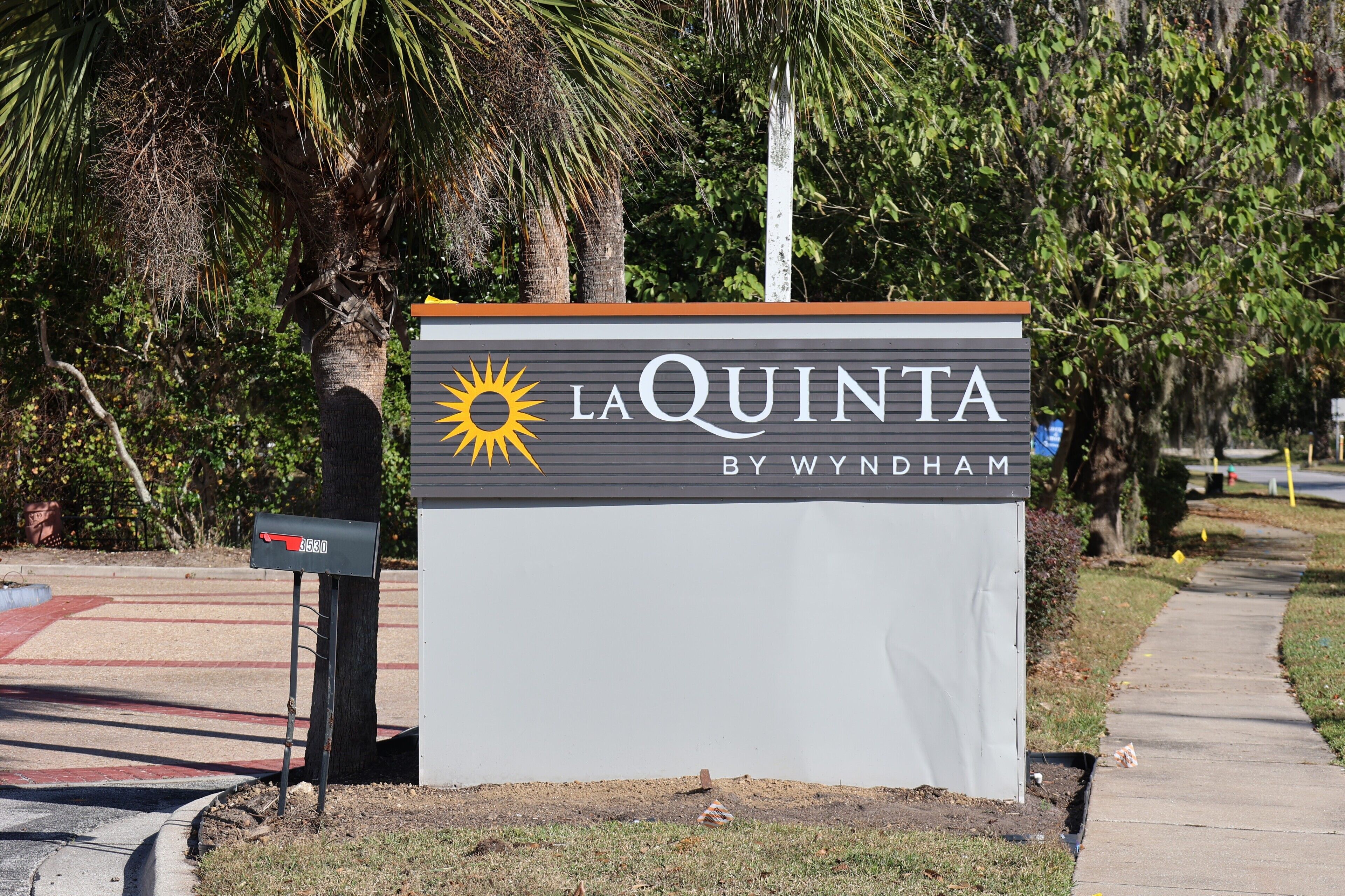 A sign for La Quinta by Wyndham with a mailbox and a sidewalk.