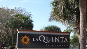Señal de La Quinta by Wyndham con un símbolo de sol, al lado de una carretera con palmeras.