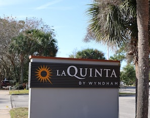 A sign for La Quinta by Wyndham with a sun symbol, located beside a road with palm trees. - La Quinta Inn & Suites by Wyndham Ocala (Ocala)