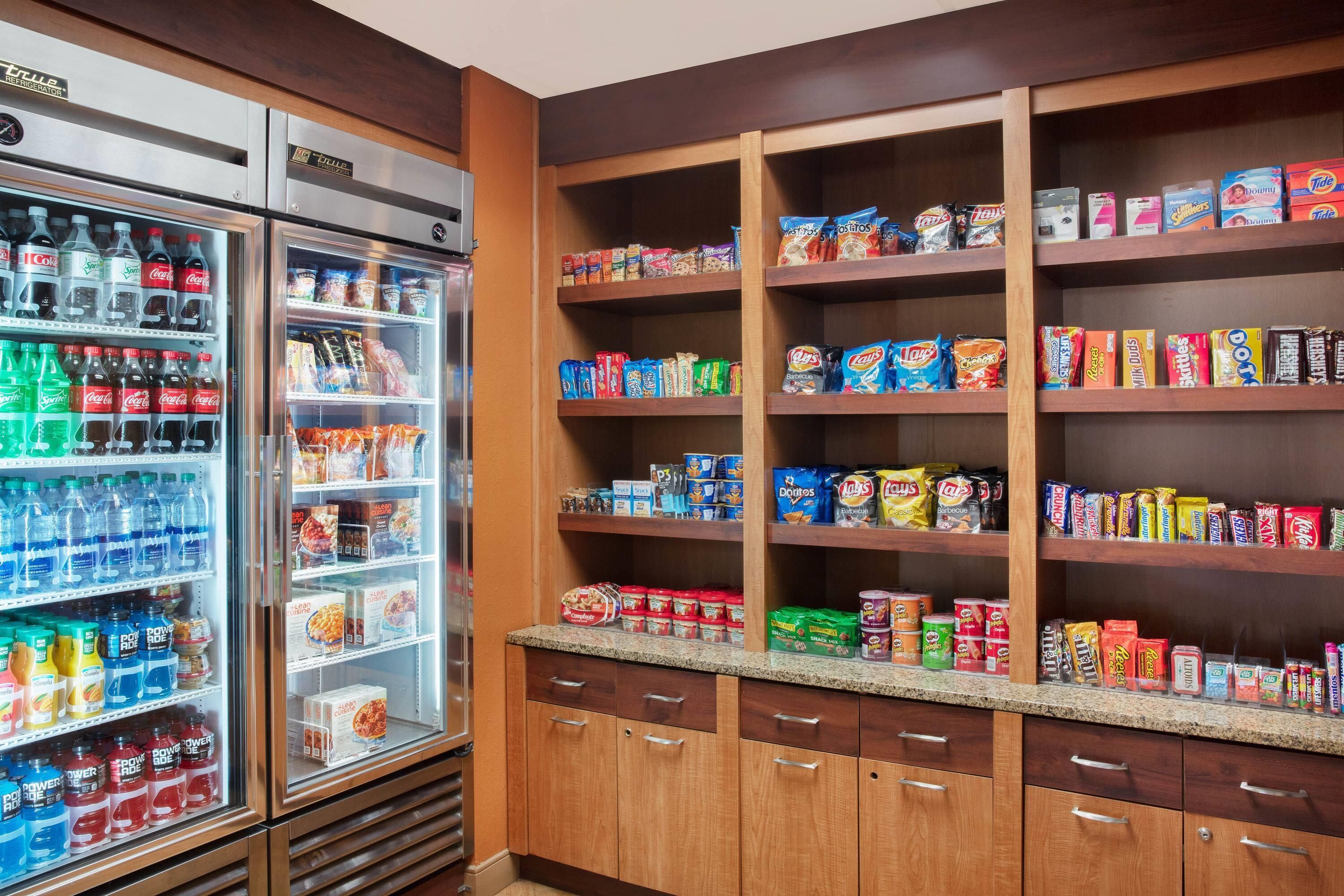 Zona de venta automática de aperitivos y bebidas, con refrigerador y estantes repletos de diversas opciones.