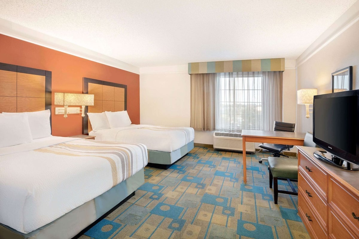 A hotel room with two beds, a desk, a television, and a window with curtains.