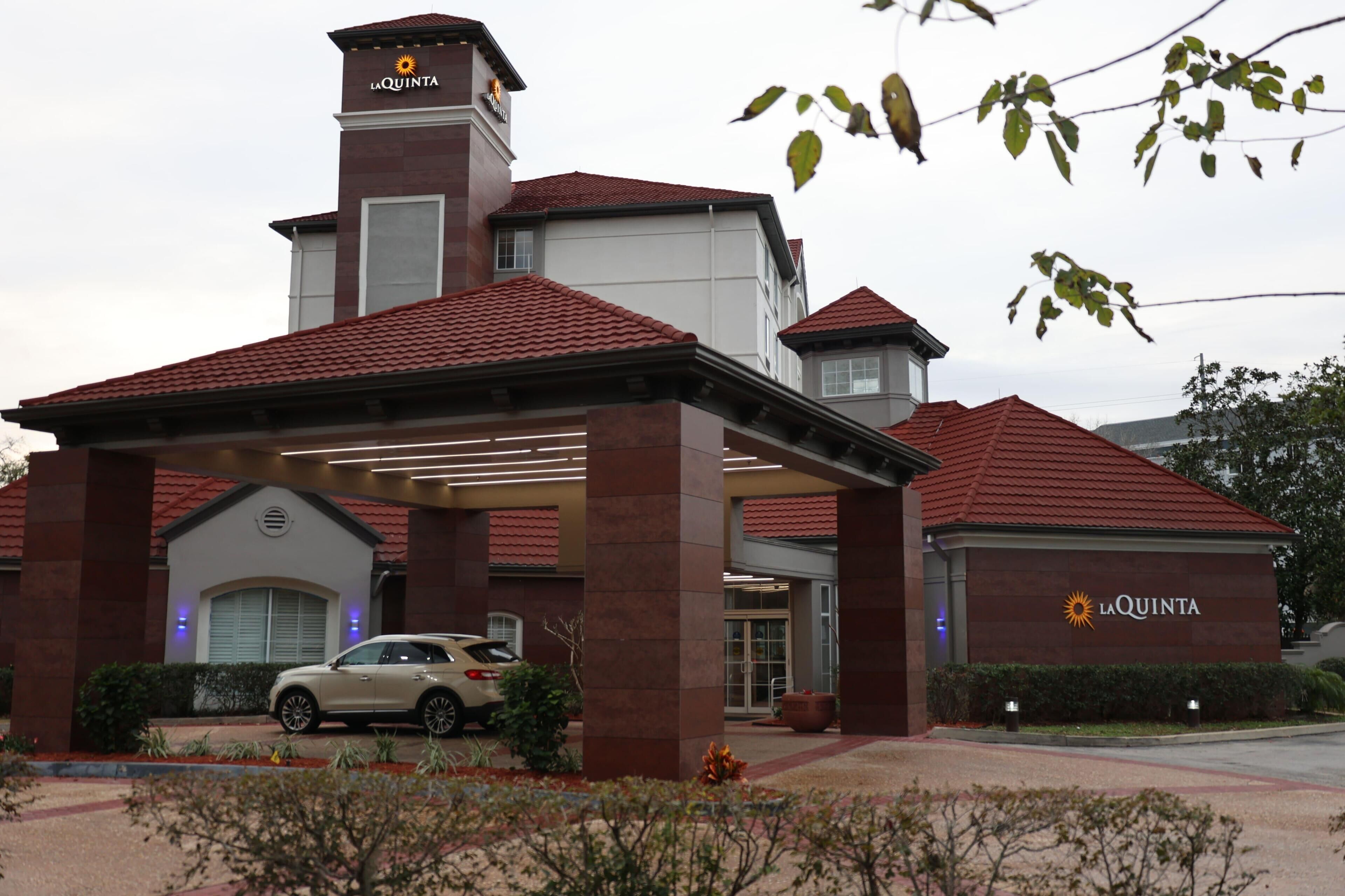 A hotel entrance with a car parked in front, a covered area, and a sign reading "La Quinta".