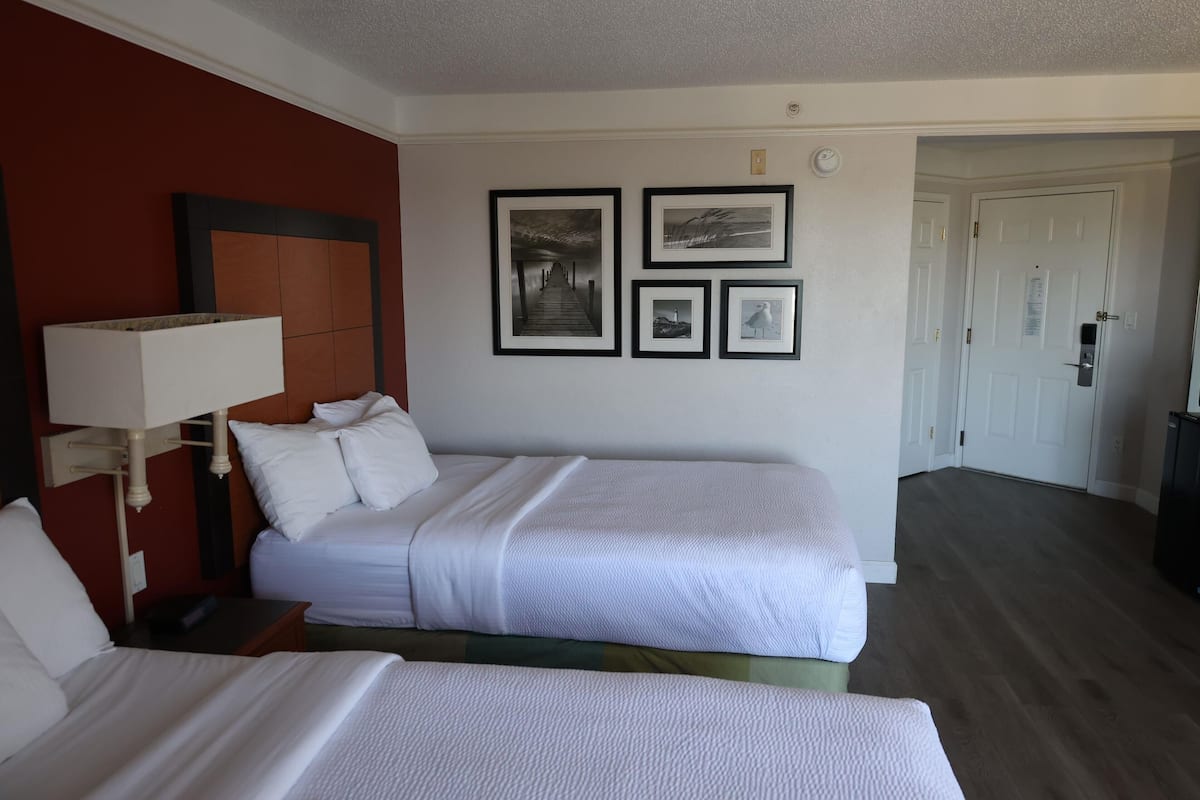 A hotel room with two beds, a nightstand, a lamp, and framed pictures on the wall.