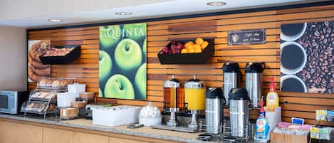 Un bar où l'on sert le petit-déjeuner, avec une enseigne indiquant qu'il sert également du café, un présentoir de fruits et différents types de machines à café.