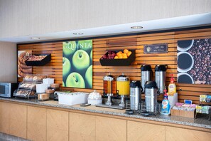 A breakfast bar with a coffee shop sign, a fruit display, and various coffee machines.