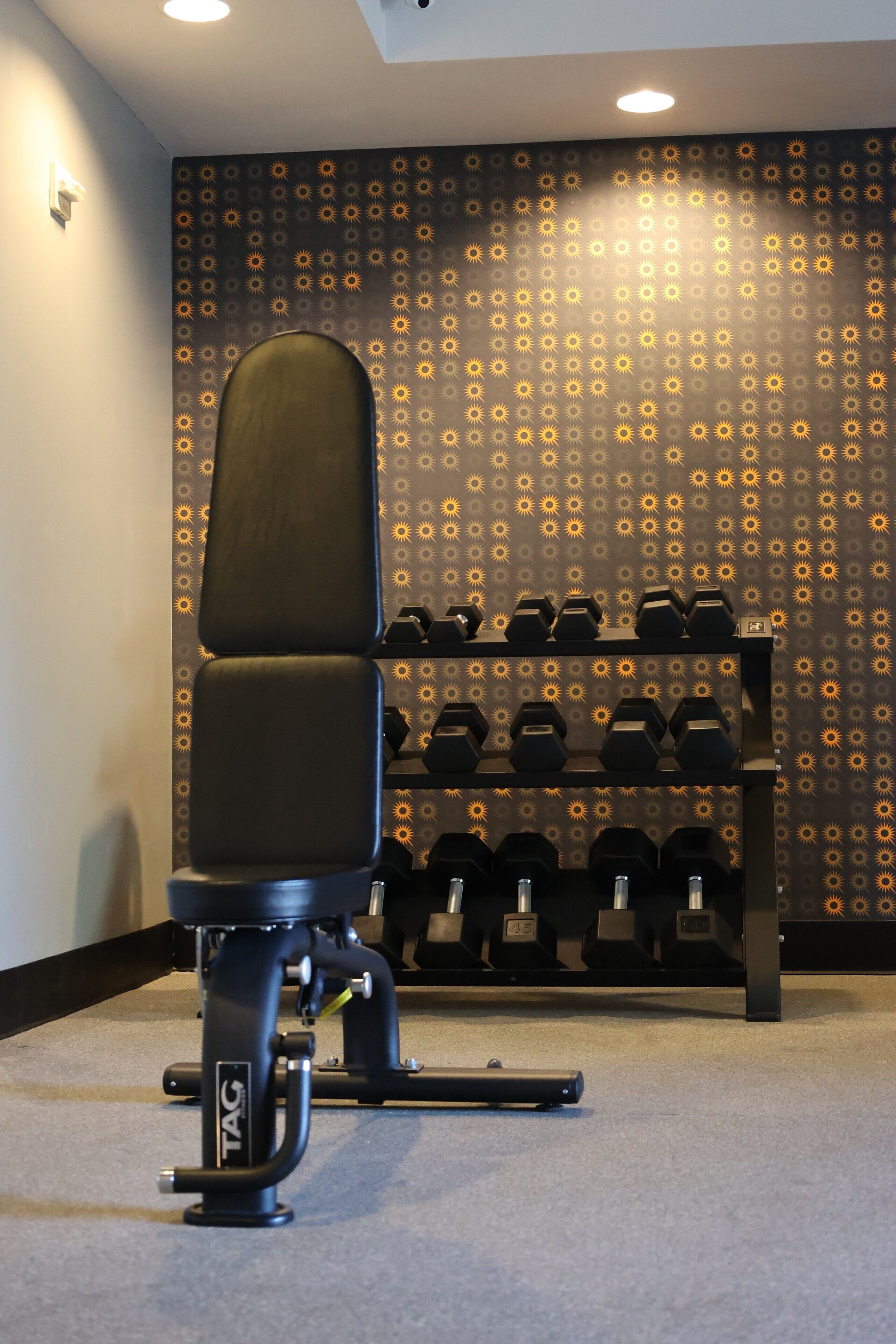 A gym with a black chair, a rack of dumbbells, and a patterned wall.