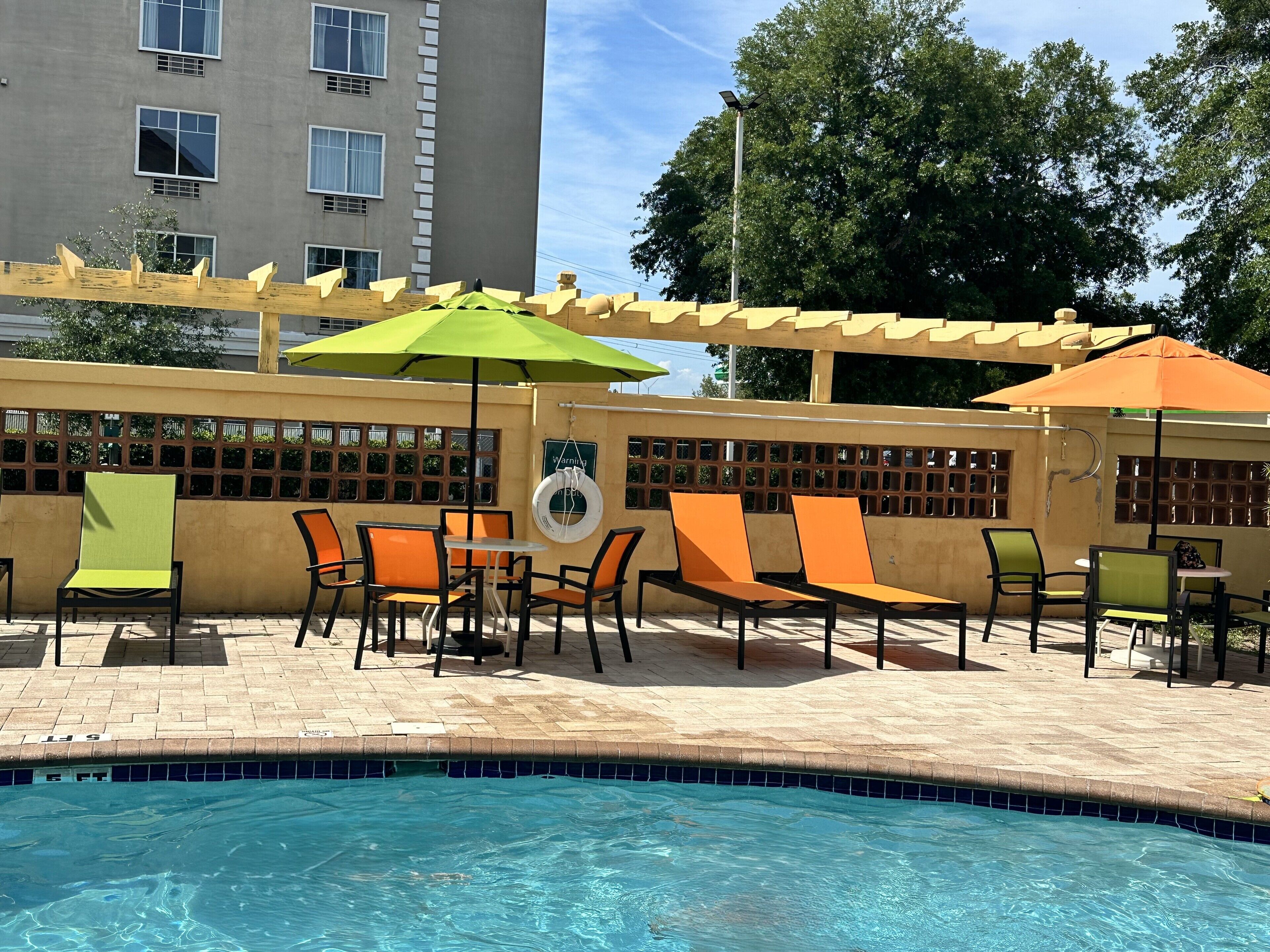 A poolside area with lounge chairs and umbrellas, a pool, and a building in the background.