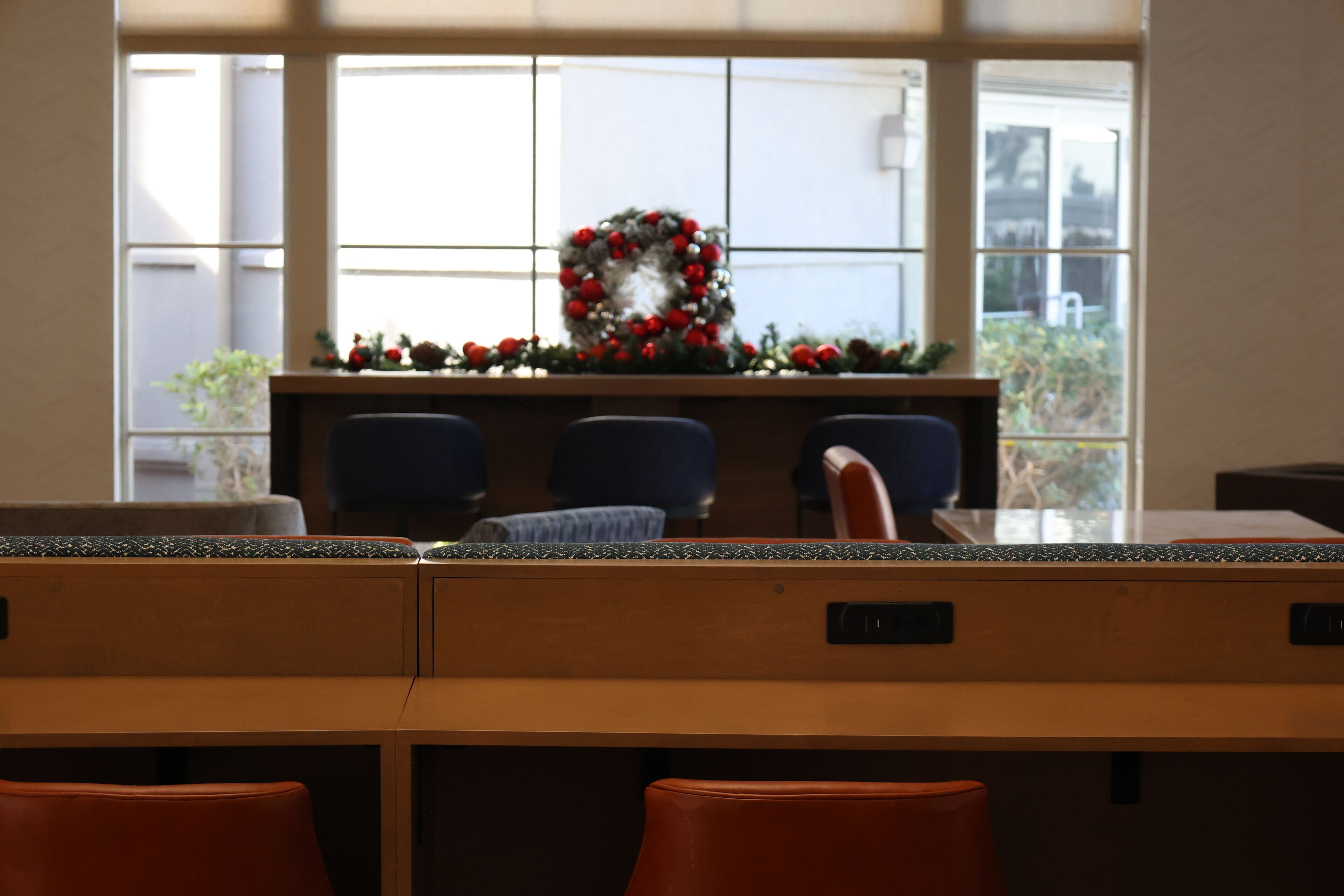 A conference room with a long table, several chairs, and a decorative wreath on a window sill.