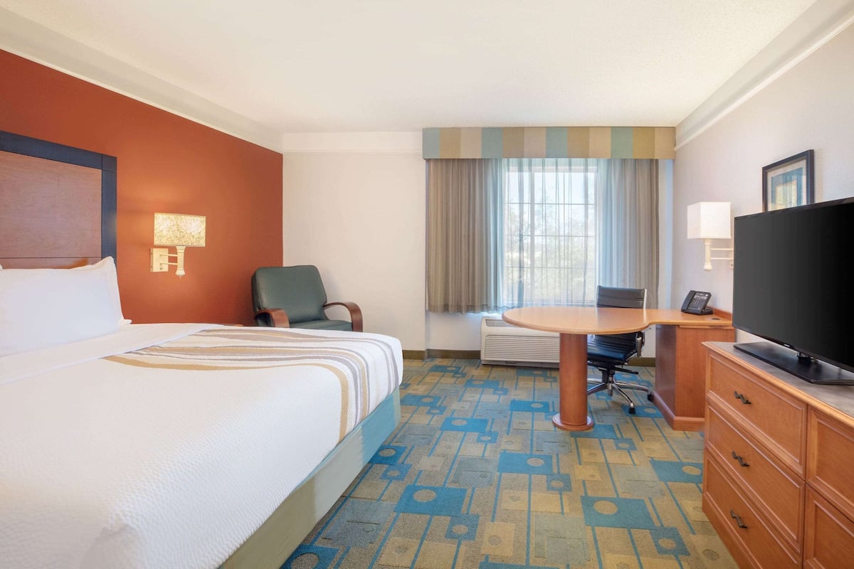 A hotel room with a bed, a desk, a television, and a window with curtains.
